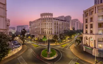 Elegant neoclassical-style building at a roundabout, illuminated at sunset, surrounded by well-planned roads and greenery.