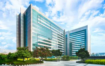 Modern glass office buildings with landscaped surroundings under a bright blue sky.