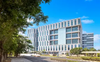 Modern office building with a sleek glass facade, surrounded by greenery and a clear blue sky.