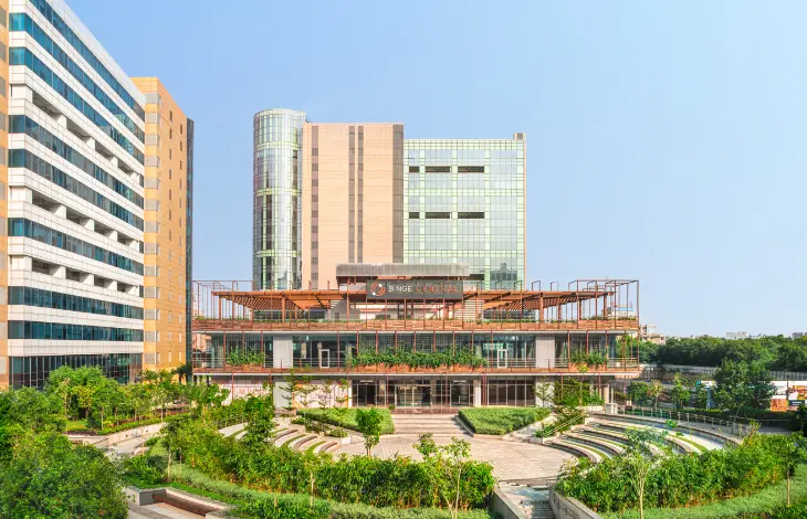 View of Candor TechSpace, Sector 62, Noida, showcasing the modern building with lush greenery and a seating area in the foreground, offering a combination of office space and outdoor relaxation.