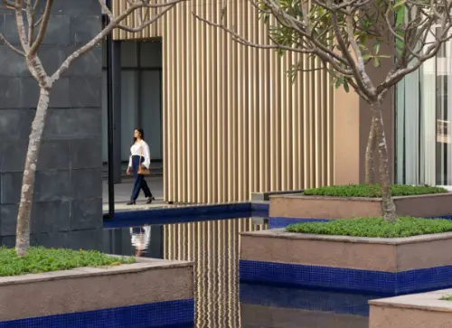 A professional walks through a serene courtyard at Candor TechSpace, Newtown, Kolkata, with lush greenery and a reflective water feature. The peaceful environment fosters a productive work atmosphere.