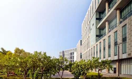 A clear view of Candor TechSpace in Sector 135, Noida, featuring modern glass buildings with lush green landscaping in the foreground and bright blue skies in the background.