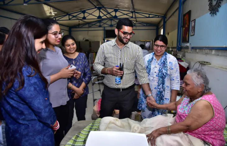 A group of individuals smiling and interacting with an elderly woman in a warm, caring environment