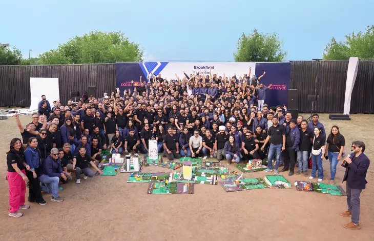 A large group of Brookfield Properties employees posing together at a team event with model structures in the foreground.