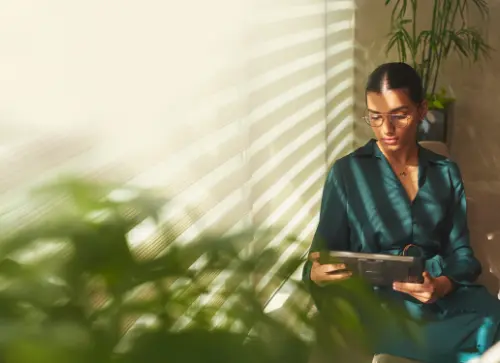 A person sitting with a tablet in a well-lit space, with sunlight streaming through blinds, at Candor TechSpace, Sector 48, Gurugram