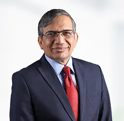 Alok Aggarwal, CEO, is pictured in a formal suit with a red tie, smiling confidently in a professional office environment, representing leadership and expertise in business management.