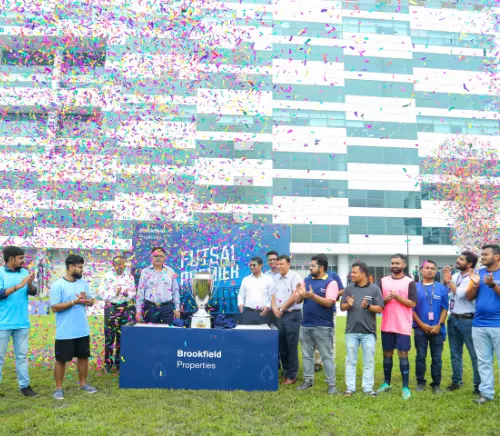 A celebration with confetti falling over a group of people at Brookfield Properties, with a trophy in the center and individuals cheering