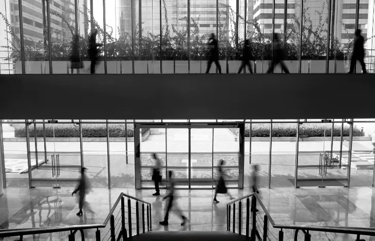 Black-and-white image of professionals walking in a modern office building at Candor TechSpace, Sector 62, Noida, with a clear view of the interior and glass walls.