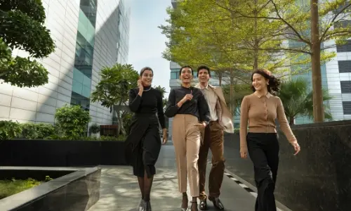 A group of professionals walking and smiling in a green outdoor space at Candor TechSpace, Sector 21, Gurugram, with modern office buildings in the background.