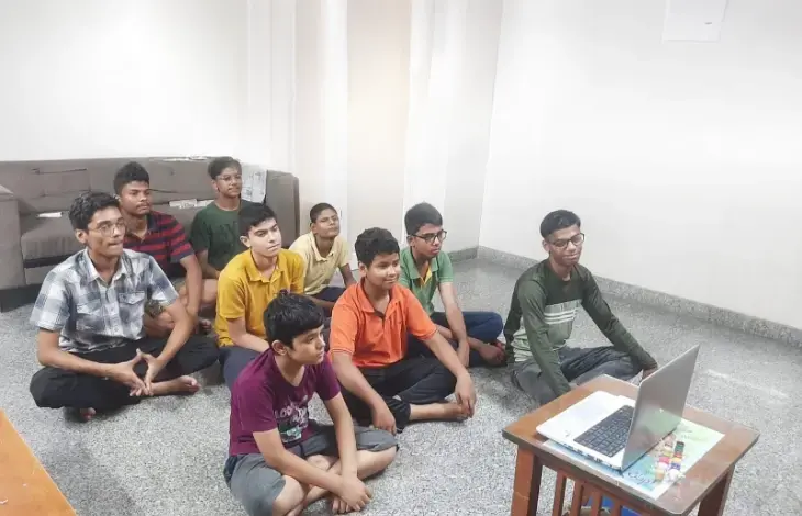 A group of children sitting on the floor, attentively watching a laptop screen during an online session or class