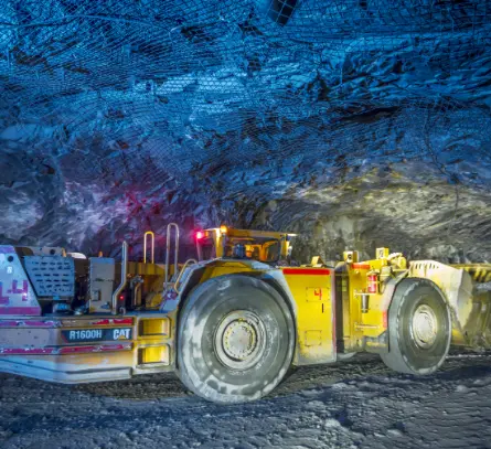 Heavy-duty underground mining truck operating inside a brightly lit blue rock mine tunnel.